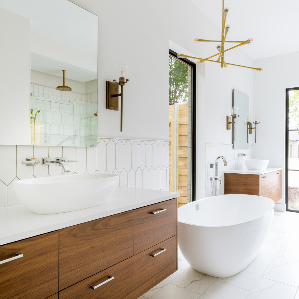 This is an example of a contemporary master bathroom in Dallas with flat-panel cabinets, medium wood cabinets, a freestanding tub, an alcove shower, white tile, white walls, a vessel sink, white floor, a hinged shower door and white benchtops.
