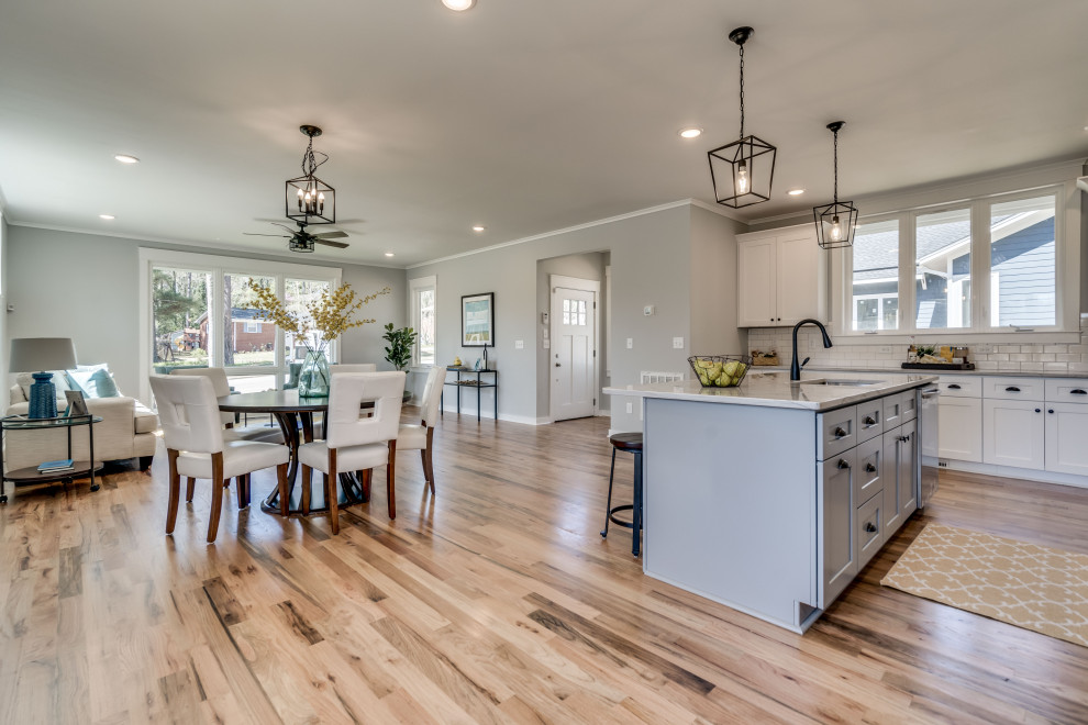 Mid-sized country eat-in kitchen in Raleigh with a single-bowl sink, shaker cabinets, white cabinets, quartzite benchtops, white splashback, subway tile splashback, stainless steel appliances, light hardwood floors, with island and white benchtop.
