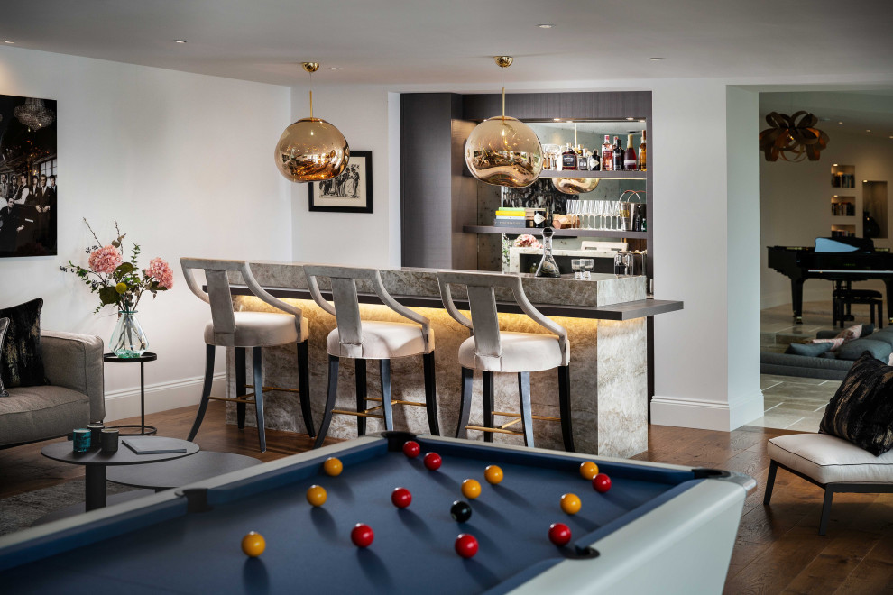 Photo of a mid-sized contemporary galley seated home bar in Cornwall with grey cabinets, mirror splashback, medium hardwood floors, brown floor and grey benchtop.