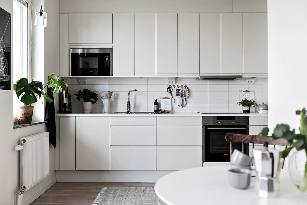 Photo of a scandinavian single-wall eat-in kitchen in Stockholm with flat-panel cabinets, grey cabinets, white splashback, subway tile splashback, stainless steel appliances, light hardwood floors, no island and beige floor.