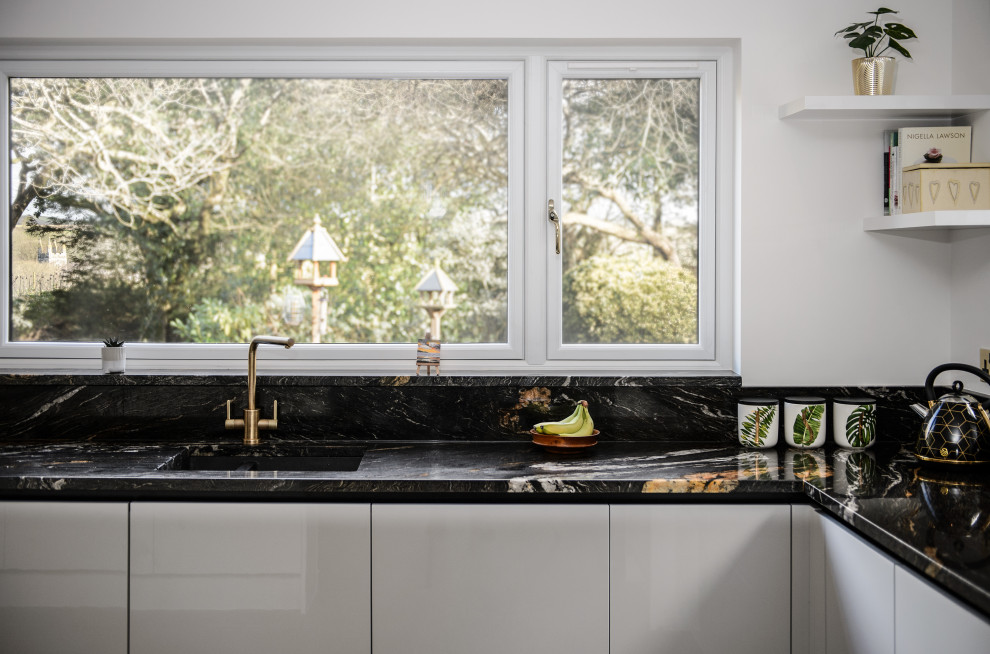 Photo of a large contemporary u-shaped eat-in kitchen in Cornwall with a drop-in sink, glass-front cabinets, white cabinets, granite benchtops, multi-coloured splashback, granite splashback, black appliances, cement tiles, a peninsula, beige floor and multi-coloured benchtop.