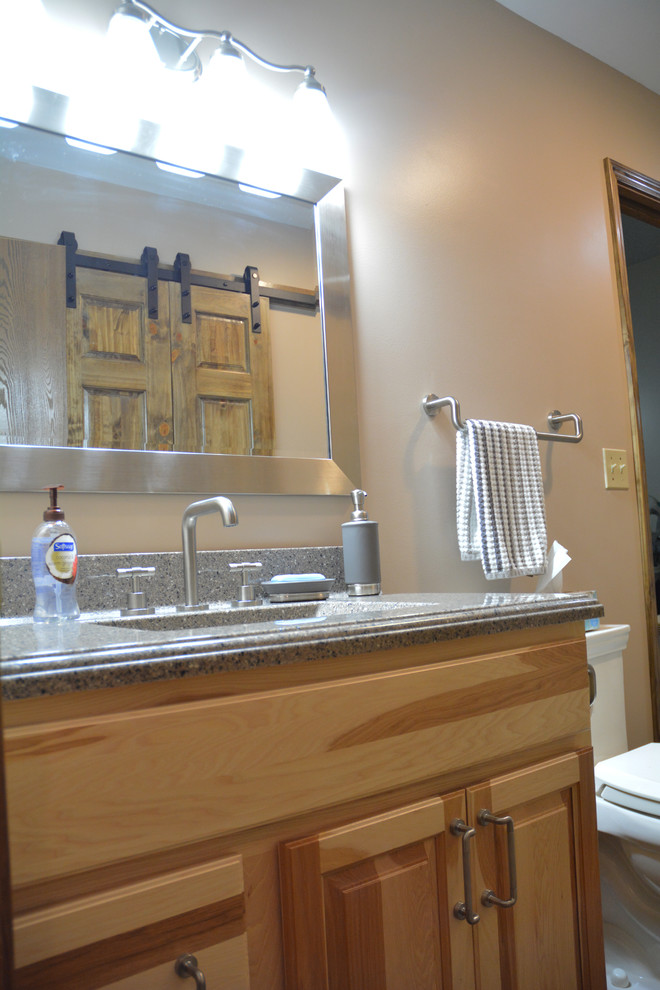 Mid-sized mountain style master brown tile and ceramic tile ceramic tile and brown floor alcove shower photo with raised-panel cabinets, light wood cabinets, a two-piece toilet, beige walls, an integrated sink, marble countertops, a hinged shower door and gray countertops