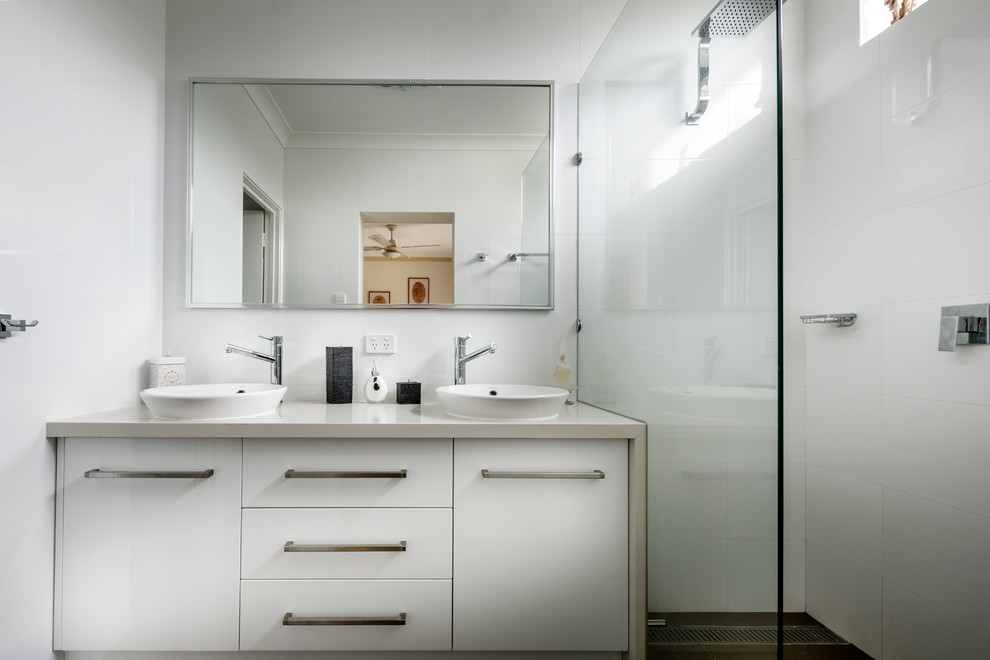Design ideas for a mid-sized contemporary bathroom in Perth with a vessel sink, recessed-panel cabinets, white cabinets, solid surface benchtops, a curbless shower, white tile, ceramic tile and white walls.