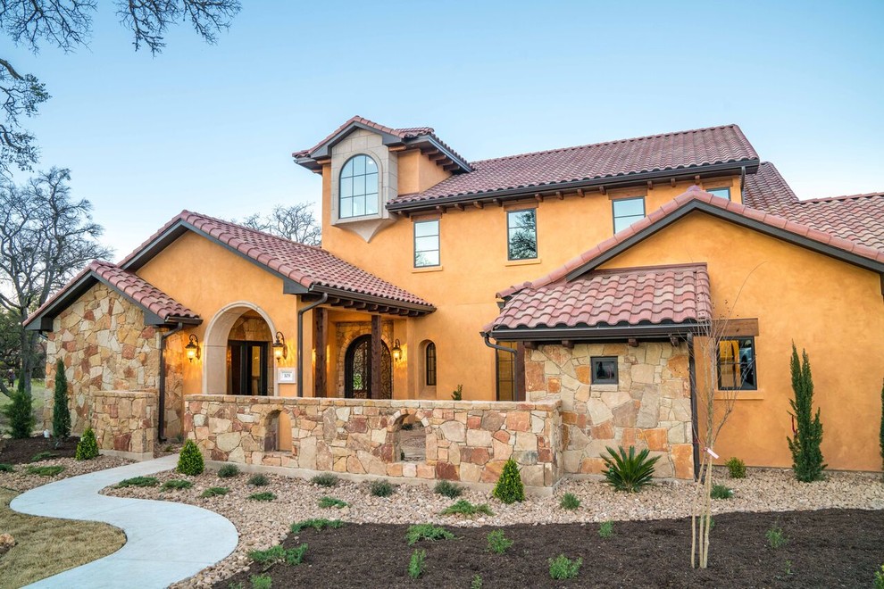This is an example of a large mediterranean two-storey adobe beige house exterior in Austin with a hip roof and a tile roof.