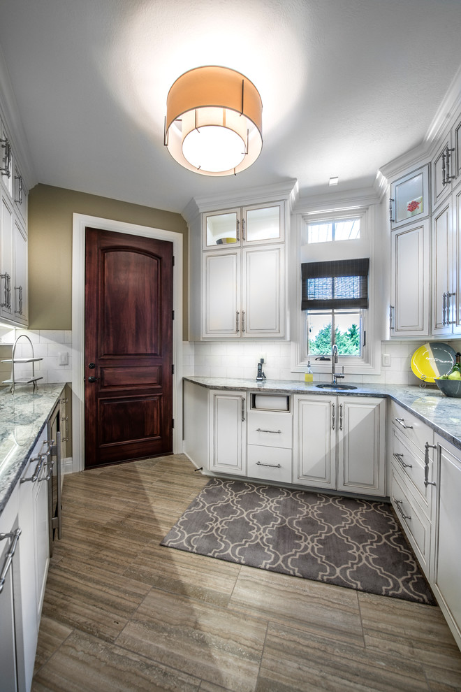 This is an example of a transitional kitchen pantry in Omaha with white splashback, an undermount sink, raised-panel cabinets, white cabinets, quartz benchtops, porcelain splashback, stainless steel appliances, porcelain floors and no island.