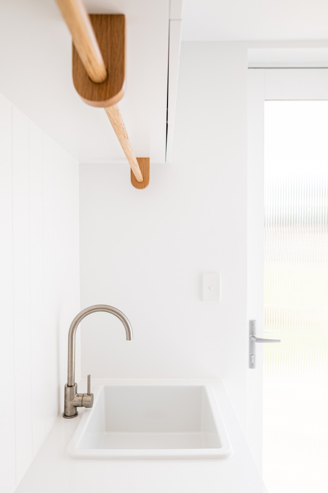 This is an example of a mid-sized beach style single-wall dedicated laundry room in Adelaide with a drop-in sink, shaker cabinets, white cabinets, laminate benchtops, white splashback, shiplap splashback, white walls, slate floors, an integrated washer and dryer, grey floor, white benchtop and decorative wall panelling.