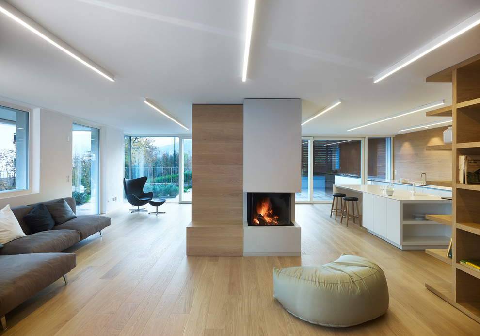 Photo of a contemporary open concept living room in Other with light hardwood floors, white walls and a plaster fireplace surround.