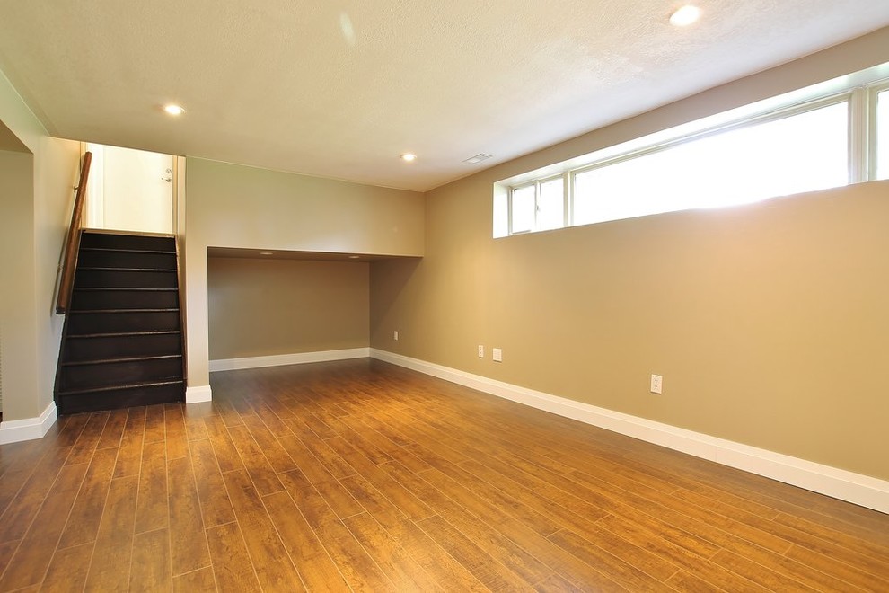 Example of a small underground medium tone wood floor basement design with beige walls, a standard fireplace and a stone fireplace
