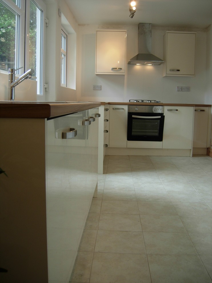 Photo of a mid-sized contemporary l-shaped separate kitchen in London with a single-bowl sink, flat-panel cabinets, black cabinets, laminate benchtops, beige splashback, ceramic splashback, stainless steel appliances, ceramic floors and no island.