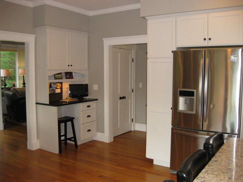 Example of a transitional l-shaped medium tone wood floor eat-in kitchen design in Boston with an undermount sink, shaker cabinets, white cabinets, granite countertops, white backsplash, ceramic backsplash, stainless steel appliances, an island and black countertops