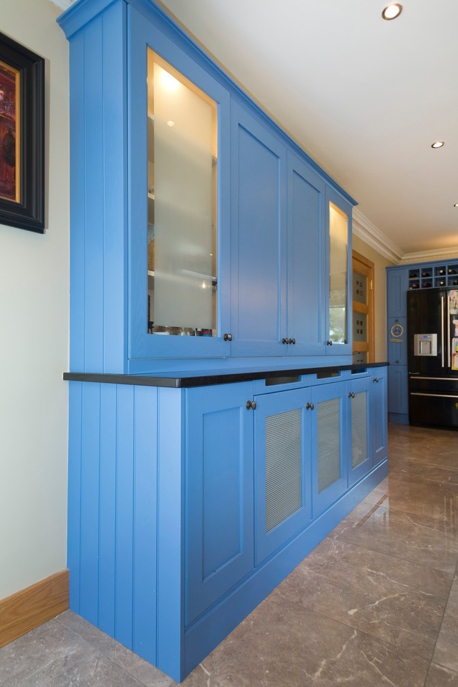 Photo of a large transitional l-shaped eat-in kitchen in Dublin with an undermount sink, shaker cabinets, blue cabinets, quartzite benchtops, black splashback, black appliances and with island.