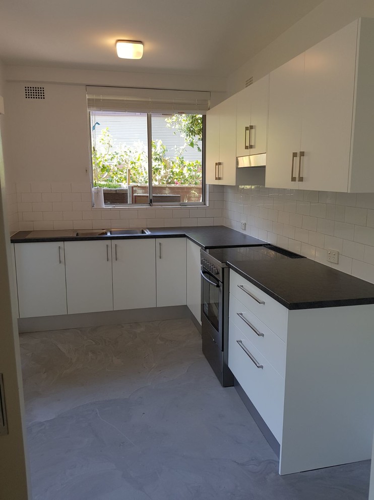 This is an example of a contemporary kitchen in Sydney with white splashback and black benchtop.