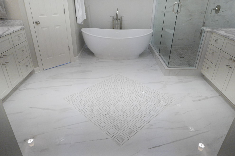 Large transitional master white tile and porcelain tile porcelain tile and white floor freestanding bathtub photo with shaker cabinets, white cabinets, a two-piece toilet, beige walls, an undermount sink, marble countertops, a hinged shower door and white countertops
