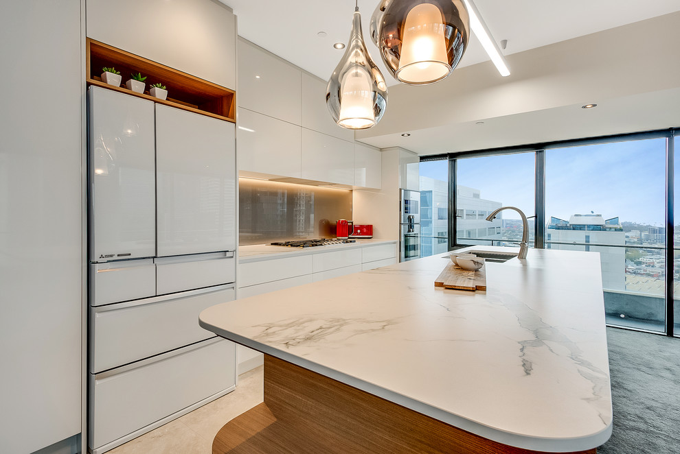 This is an example of a mid-sized modern single-wall eat-in kitchen in Melbourne with a double-bowl sink, quartz benchtops, glass sheet splashback, travertine floors, flat-panel cabinets, white cabinets, brown splashback, white appliances and with island.