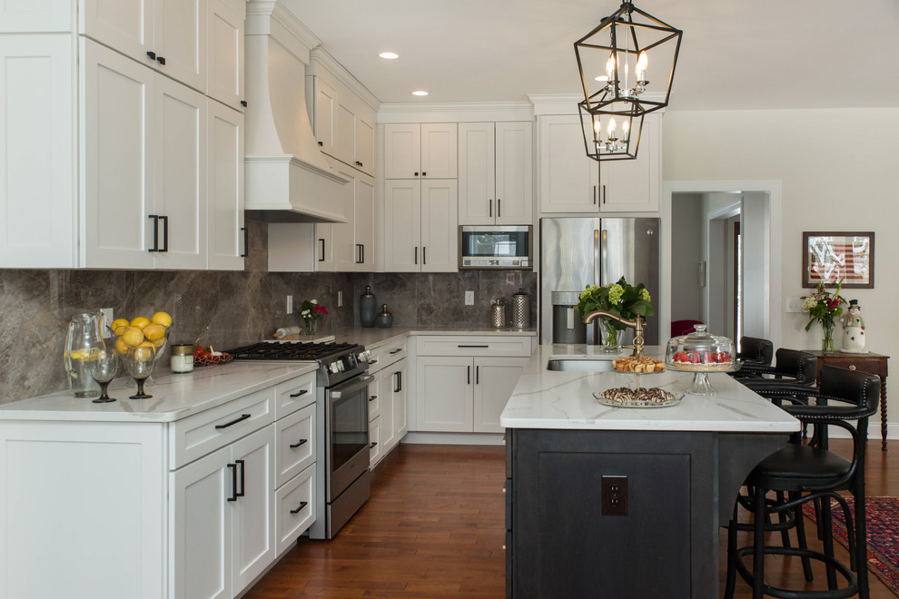 This is an example of a traditional l-shaped open plan kitchen in Boston with an undermount sink, shaker cabinets, white cabinets, grey splashback, stainless steel appliances, medium hardwood floors, with island and brown floor.