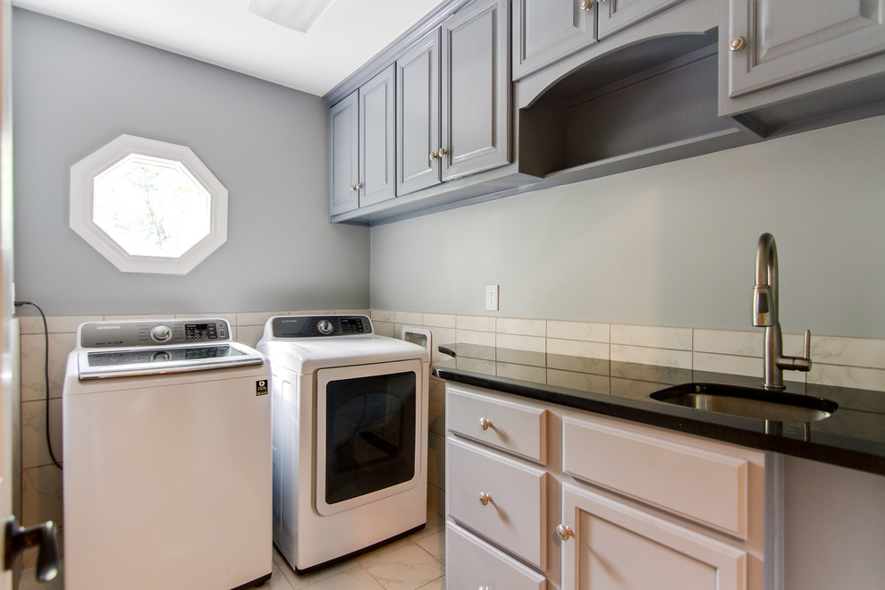 Photo of a mid-sized traditional l-shaped laundry room in Louisville with an undermount sink, raised-panel cabinets, grey cabinets, granite benchtops, grey walls, marble floors, a side-by-side washer and dryer, white floor and black benchtop.