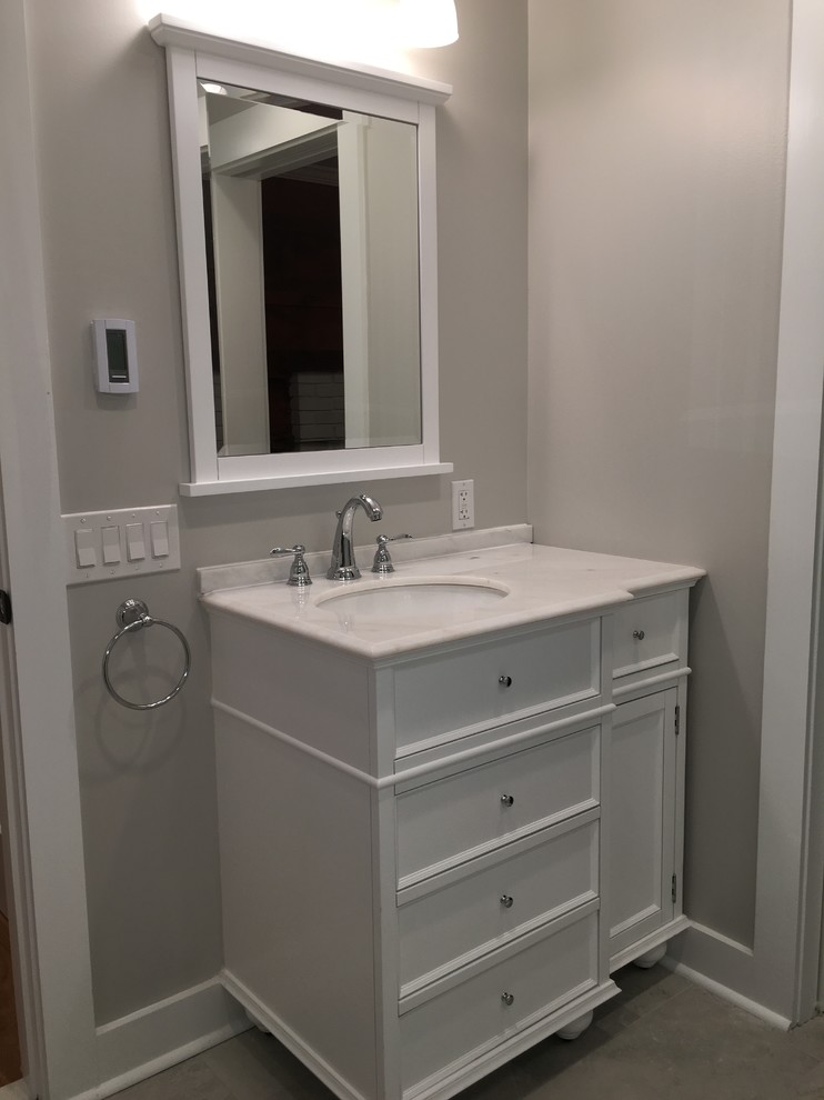 This is an example of a mid-sized transitional 3/4 bathroom in New York with recessed-panel cabinets, white cabinets, an alcove shower, a one-piece toilet, white tile, subway tile, grey walls, ceramic floors, an undermount sink, marble benchtops, grey floor, a hinged shower door and yellow benchtops.