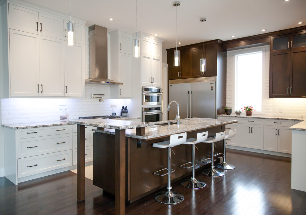 Example of a large transitional u-shaped dark wood floor and brown floor kitchen design in Calgary with an undermount sink, shaker cabinets, white cabinets, granite countertops, white backsplash, subway tile backsplash, stainless steel appliances and an island