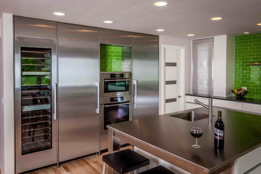 This is an example of a large contemporary u-shaped eat-in kitchen in Seattle with an undermount sink, flat-panel cabinets, white cabinets, quartz benchtops, green splashback, glass tile splashback, stainless steel appliances, light hardwood floors and with island.