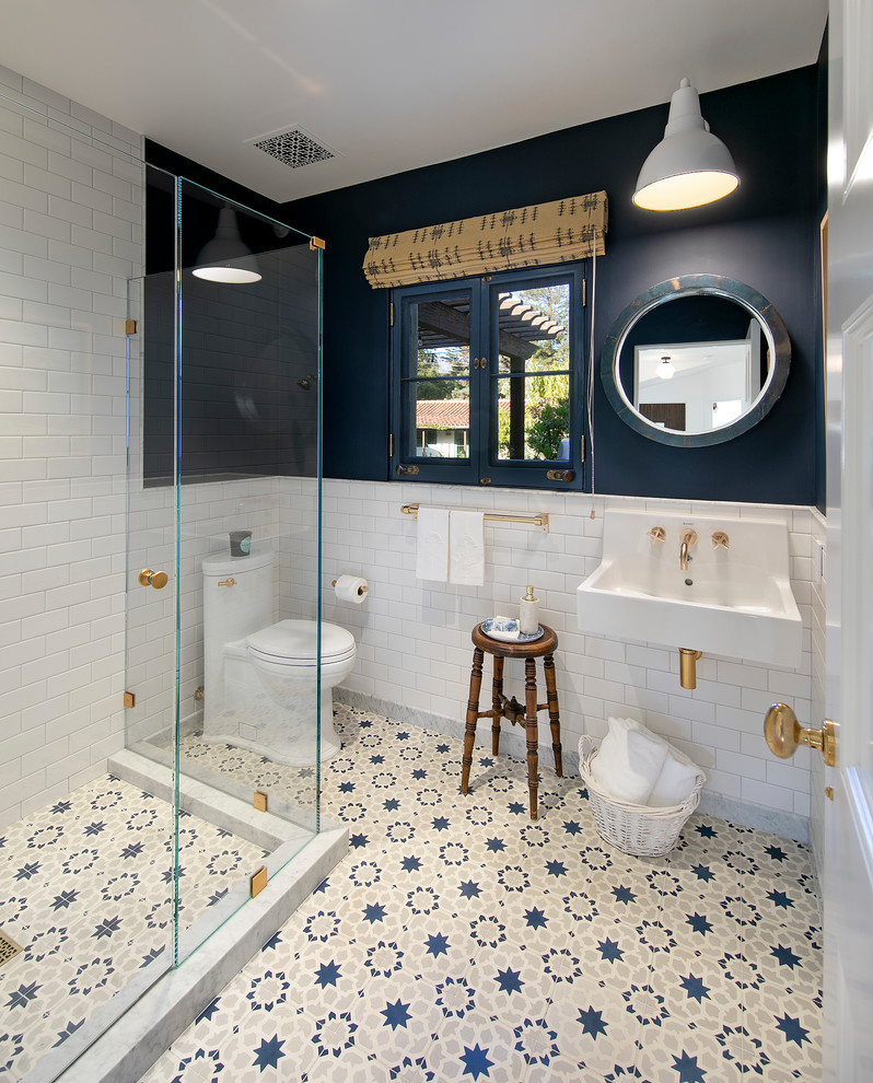 This is an example of a mid-sized mediterranean 3/4 bathroom in Santa Barbara with a corner shower, a one-piece toilet, white tile, ceramic tile, blue walls, a wall-mount sink, blue floor and a hinged shower door.