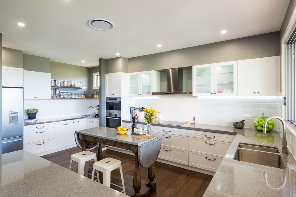 This is an example of a mid-sized industrial u-shaped kitchen in Brisbane with an undermount sink, recessed-panel cabinets, white cabinets, quartz benchtops, white splashback, subway tile splashback, stainless steel appliances, dark hardwood floors and with island.