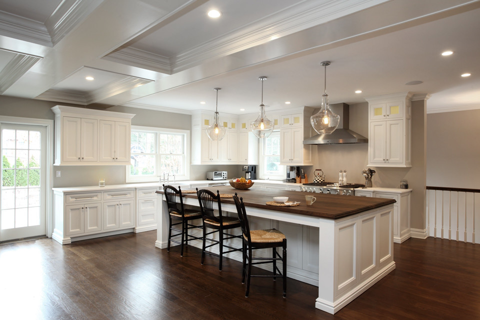 Eat-in kitchen - large transitional l-shaped medium tone wood floor eat-in kitchen idea in New York with recessed-panel cabinets, white cabinets, wood countertops, stainless steel appliances, an island, a farmhouse sink and gray backsplash