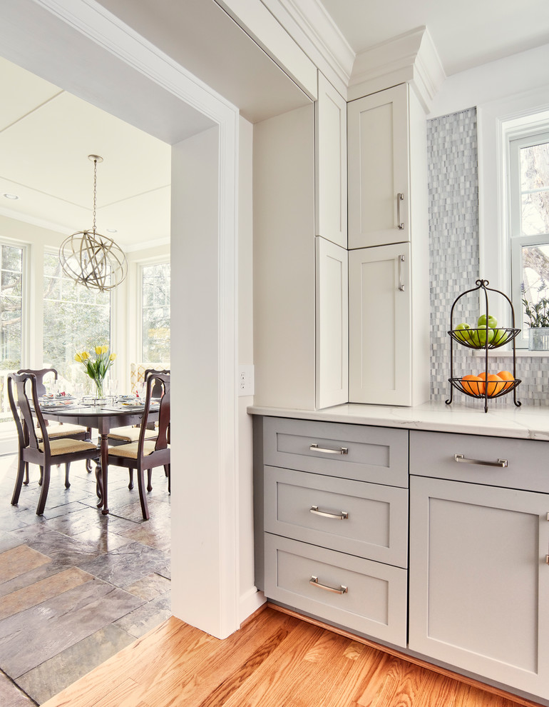 Example of a mid-sized transitional u-shaped medium tone wood floor and brown floor enclosed kitchen design with an undermount sink, shaker cabinets, gray cabinets, quartz countertops, multicolored backsplash, glass sheet backsplash, stainless steel appliances, an island and white countertops