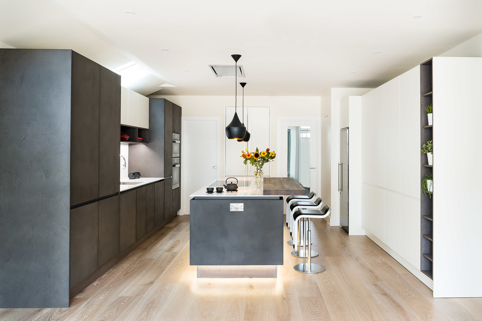 This is an example of a large modern galley kitchen in London with flat-panel cabinets, black cabinets, light hardwood floors, with island, beige floor and white benchtop.