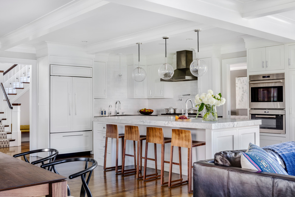 This is an example of a large transitional l-shaped open plan kitchen in Boston with a single-bowl sink, recessed-panel cabinets, white cabinets, soapstone benchtops, white splashback, stone tile splashback, stainless steel appliances, medium hardwood floors, with island and brown floor.