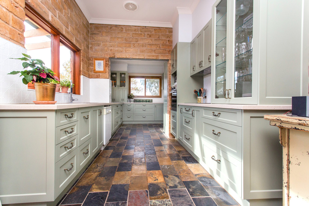 Photo of a small country galley kitchen in Other with a double-bowl sink, shaker cabinets, green cabinets, solid surface benchtops, white splashback, metal splashback, slate floors, multi-coloured floor and beige benchtop.