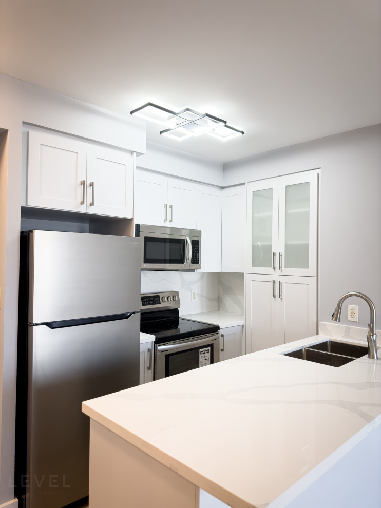 Mid-sized contemporary u-shaped eat-in kitchen in Toronto with an undermount sink, shaker cabinets, white cabinets, quartz benchtops, white splashback, engineered quartz splashback, stainless steel appliances, vinyl floors, a peninsula, brown floor and white benchtop.