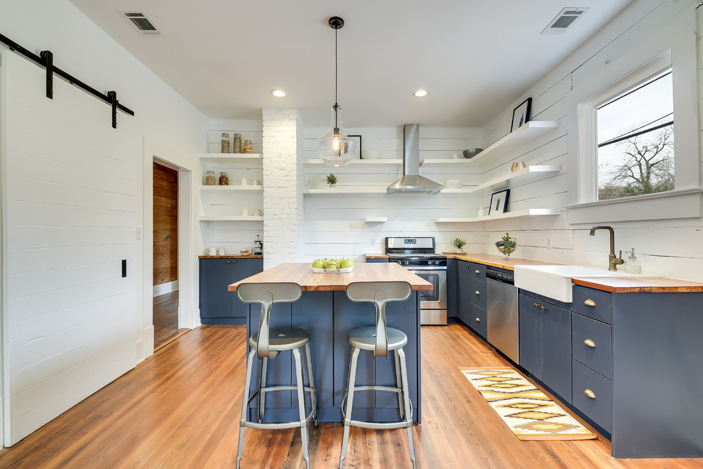 Photo of a transitional l-shaped kitchen in Austin with a farmhouse sink, flat-panel cabinets, blue cabinets, white splashback, stainless steel appliances, medium hardwood floors, with island and brown floor.