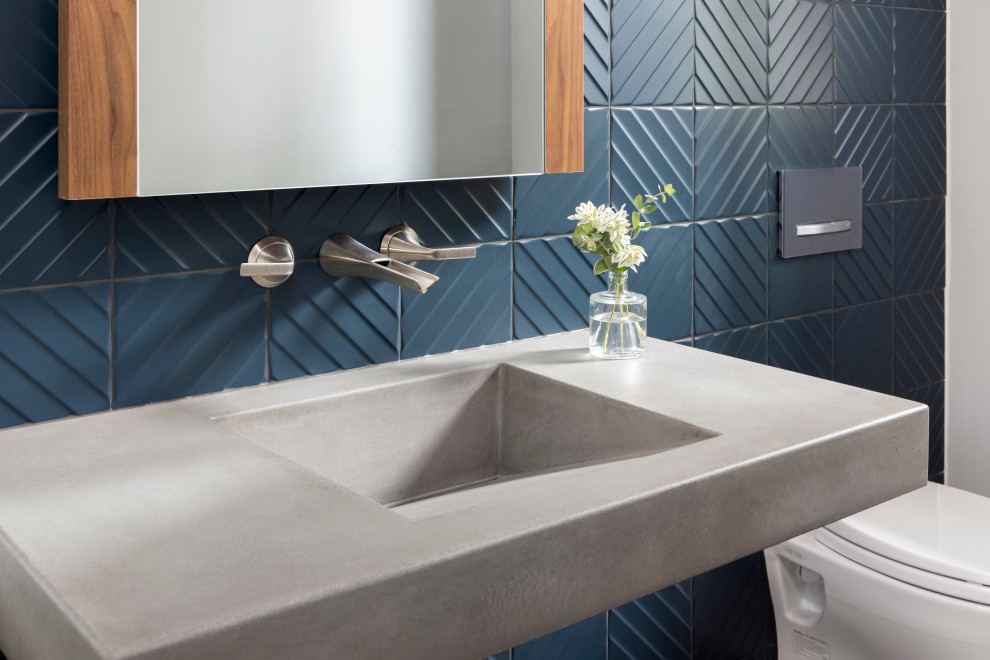 Inspiration för ett mellanstort funkis grå grått toalett, med grå skåp, en vägghängd toalettstol, blå kakel, keramikplattor, vita väggar, mellanmörkt trägolv, ett integrerad handfat, bänkskiva i betong och brunt golv
