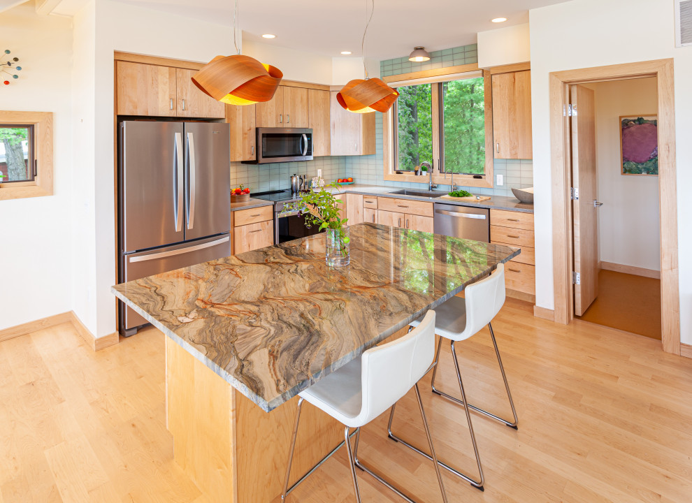 Mid-sized midcentury l-shaped eat-in kitchen in Detroit with an undermount sink, flat-panel cabinets, light wood cabinets, quartzite benchtops, green splashback, glass tile splashback, stainless steel appliances, light hardwood floors, with island, brown floor and grey benchtop.