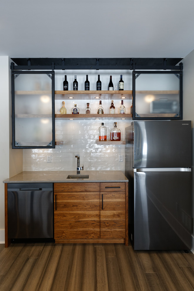 This is an example of a contemporary wet bar in Cincinnati with flat-panel cabinets, medium wood cabinets, white splashback, brown floor, an undermount sink, quartzite benchtops, ceramic splashback, medium hardwood floors and grey benchtop.