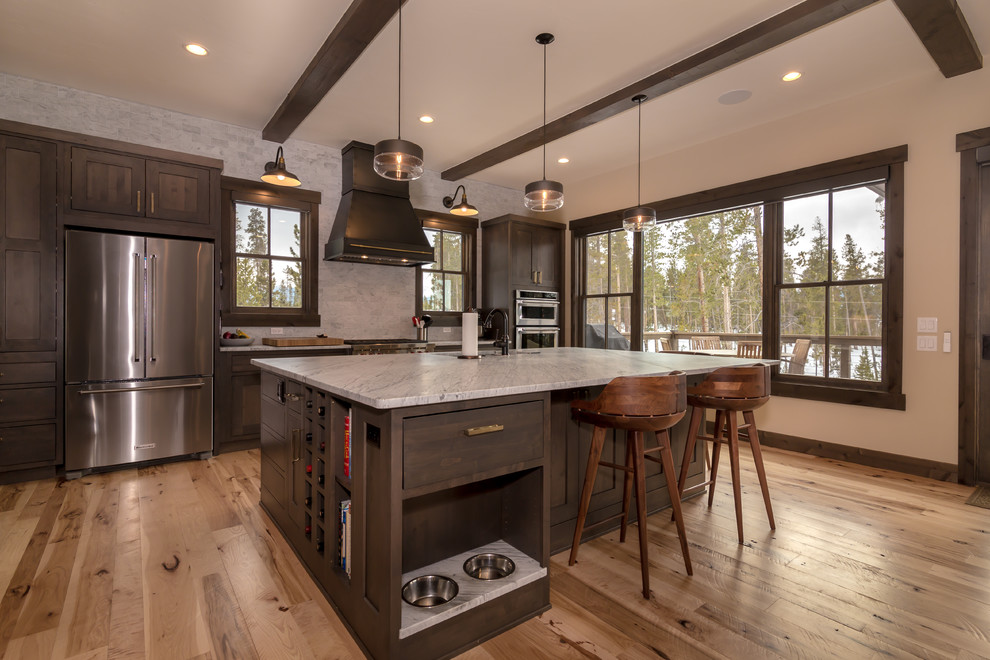 Example of a large mountain style l-shaped light wood floor and beige floor open concept kitchen design in Denver with an undermount sink, shaker cabinets, dark wood cabinets, quartz countertops, beige backsplash, subway tile backsplash, stainless steel appliances, an island and white countertops