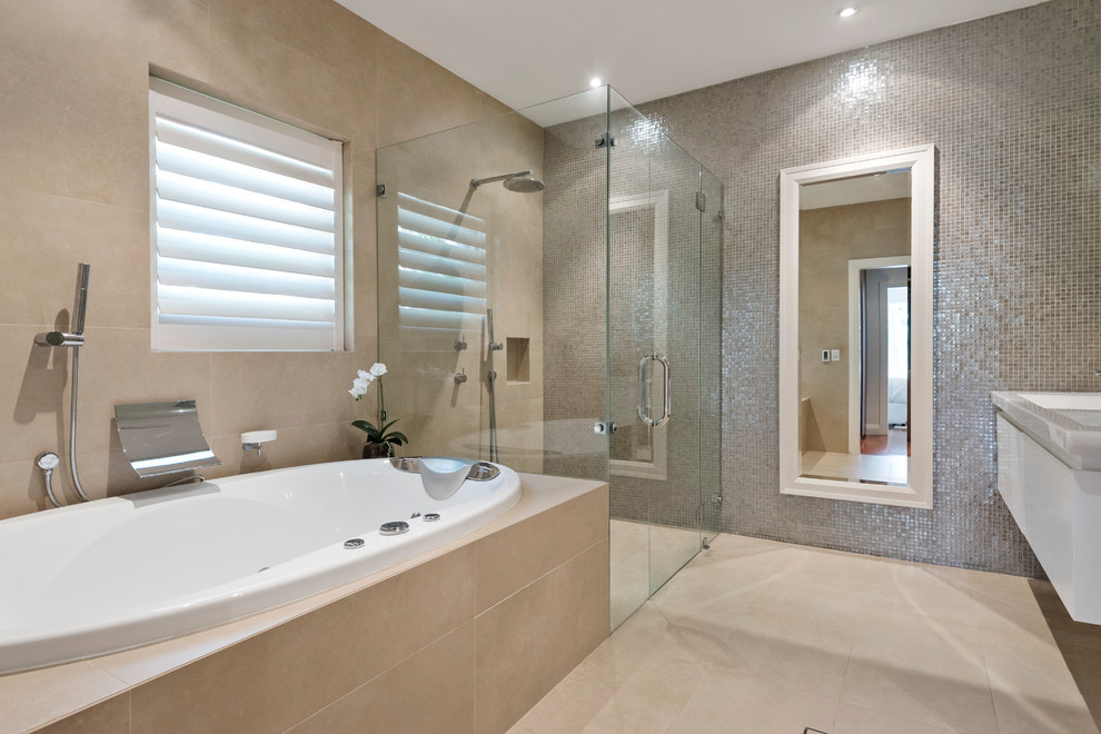 Inspiration for a large modern master bathroom in Sydney with flat-panel cabinets, white cabinets, a drop-in tub, a wall-mount toilet, beige tile, stone tile, beige walls, porcelain floors, an integrated sink, solid surface benchtops, beige floor, a hinged shower door and white benchtops.
