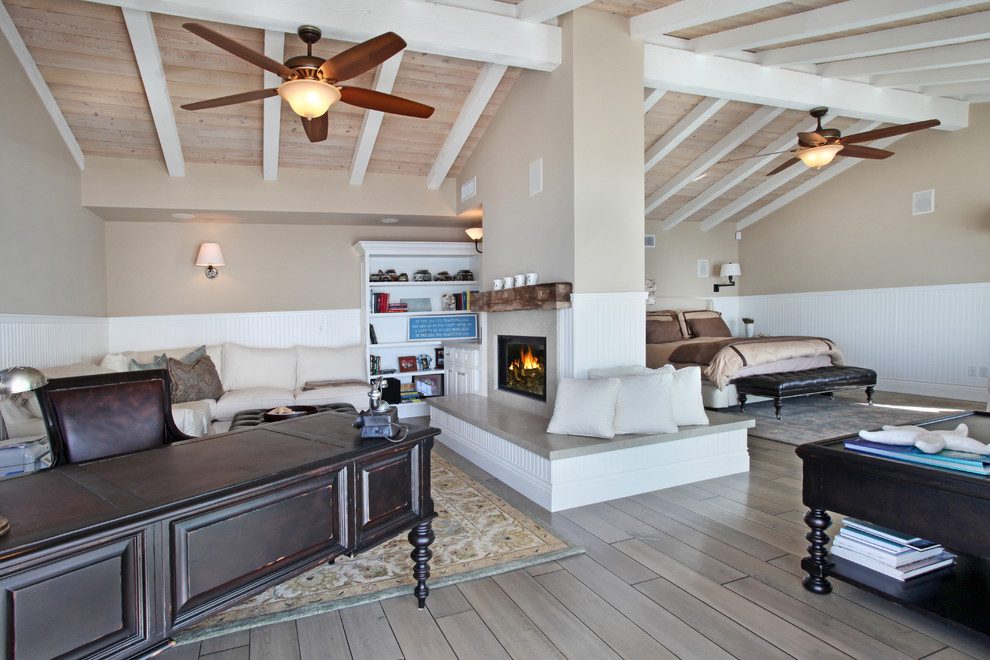 This is an example of a beach style bedroom in Orange County with beige walls, medium hardwood floors and a two-sided fireplace.