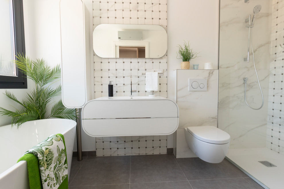 Mid-sized modern master bathroom in Malaga with white cabinets, a freestanding tub, a wall-mount toilet, black and white tile, porcelain tile, white walls, porcelain floors, a drop-in sink, solid surface benchtops, grey floor, white benchtops, a single vanity and a floating vanity.