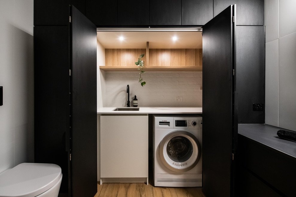 Inspiration for a large contemporary galley utility room in Melbourne with porcelain floors, brown floor, a drop-in sink, open cabinets, light wood cabinets, laminate benchtops, white walls, an integrated washer and dryer and white benchtop.