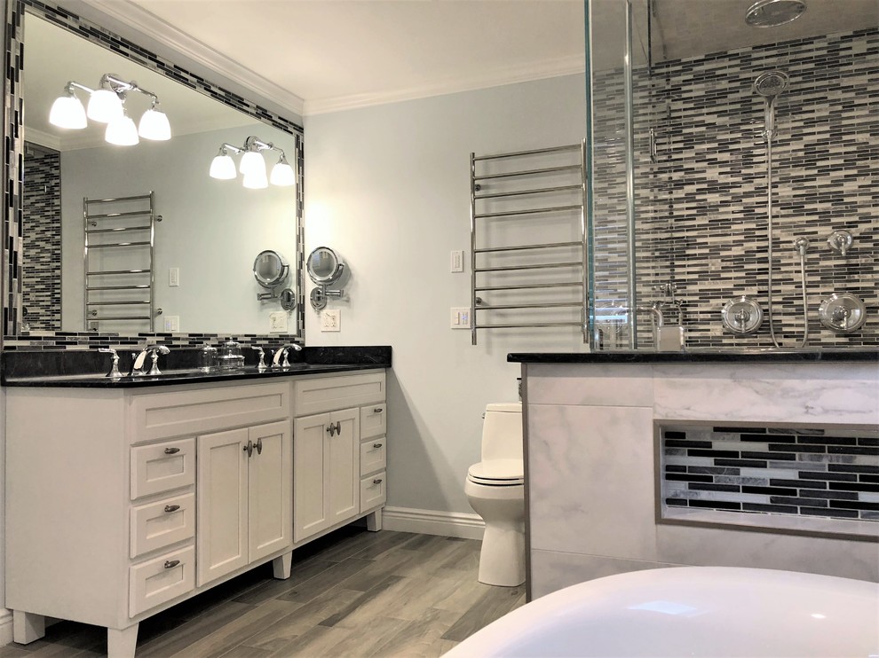 Photo of a mid-sized transitional master bathroom in Bridgeport with shaker cabinets, white cabinets, a freestanding tub, a double shower, a one-piece toilet, gray tile, porcelain tile, blue walls, porcelain floors, an integrated sink, solid surface benchtops, grey floor and a hinged shower door.
