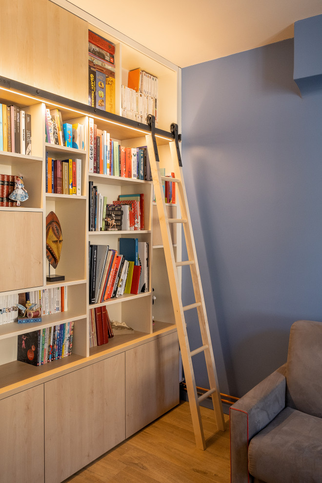 Cette photo montre un grand salon tendance fermé avec une bibliothèque ou un coin lecture, un mur bleu, un sol en bois brun et un sol marron.