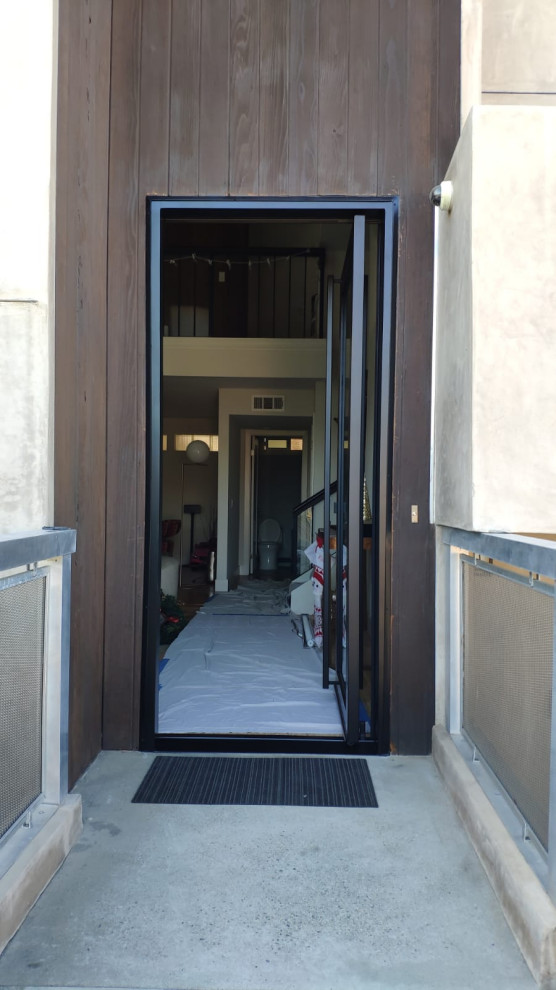 Exemple d'une petite porte d'entrée tendance en bois avec un mur marron, sol en béton ciré, une porte pivot, une porte noire et un sol gris.