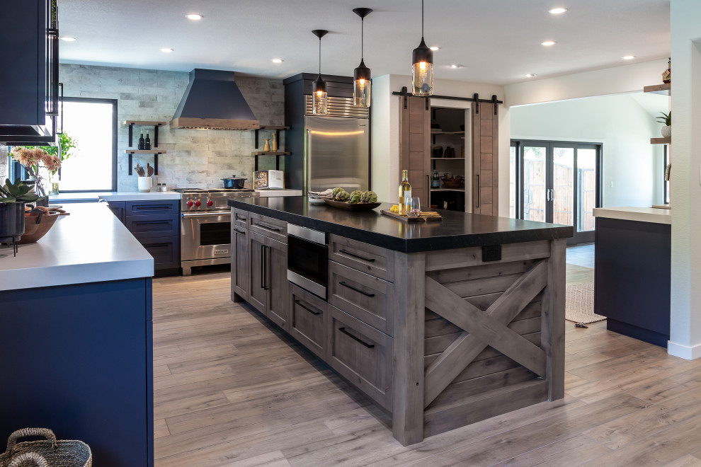 Large industrial l-shaped eat-in kitchen in San Francisco with an undermount sink, shaker cabinets, black cabinets, granite benchtops, stone slab splashback, stainless steel appliances, laminate floors, with island, brown floor and black benchtop.