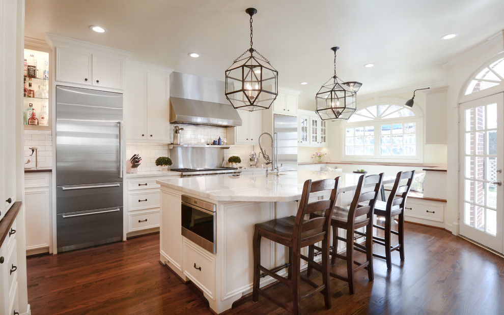 This is an example of a large traditional l-shaped eat-in kitchen in Houston with a farmhouse sink, recessed-panel cabinets, white cabinets, quartzite benchtops, white splashback, stainless steel appliances, dark hardwood floors, with island and subway tile splashback.