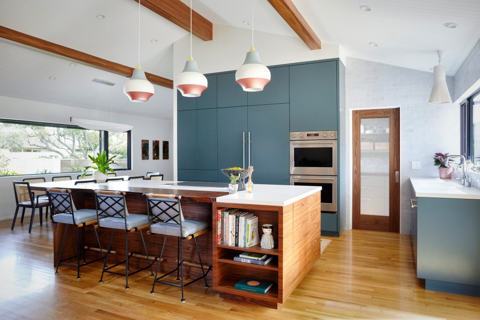 Foto på ett 50 tals vit kök, med en nedsänkt diskho, släta luckor, blå skåp, bänkskiva i kvarts, vitt stänkskydd, stänkskydd i tunnelbanekakel, integrerade vitvaror, ljust trägolv och en köksö