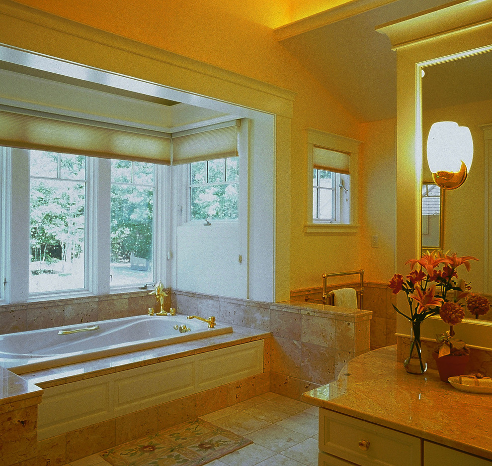 This is an example of a large mediterranean master bathroom in Portland Maine with recessed-panel cabinets, white cabinets, a drop-in tub, beige walls, travertine floors and marble benchtops.