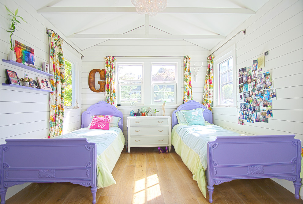 This is an example of a beach style kids' room for girls in San Francisco with white walls and light hardwood floors.
