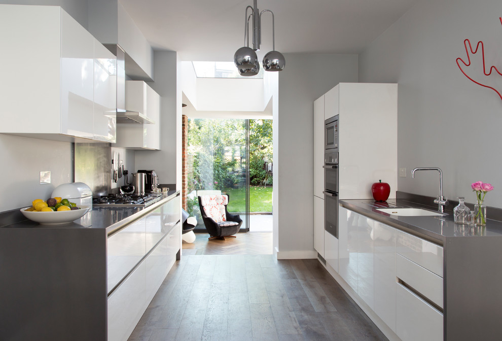 This is an example of a small contemporary galley kitchen in London with an undermount sink, flat-panel cabinets, white cabinets, stainless steel appliances, no island, grey floor, grey benchtop and medium hardwood floors.