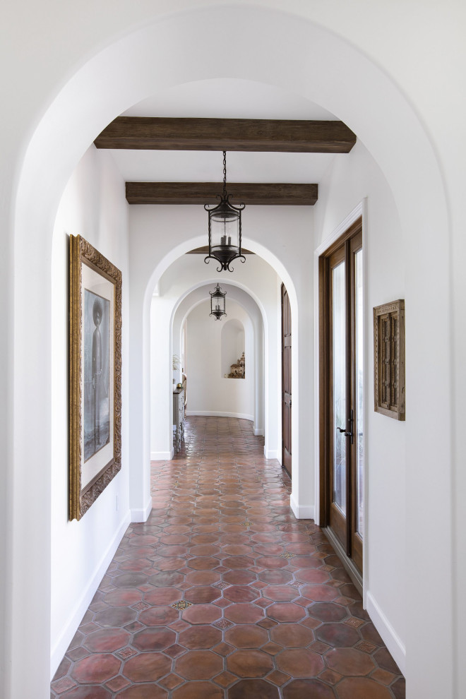 Design ideas for a large mediterranean hallway in San Diego with white walls, terra-cotta floors, brown floor and exposed beam.
